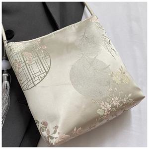 Close-up of elegant floral embroidery and tassel detail on a champagne silk bucket bag