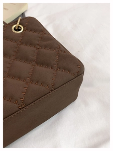 Detail of dark brown quilted crossbody bag with golden eyelet and suede-like texture