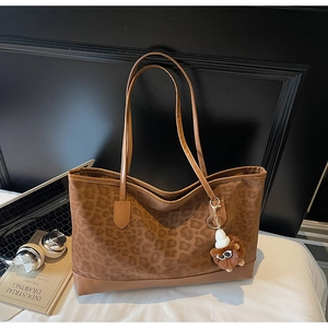 Detail of leopard print tote bag with plush lion charm next to a laptop and book