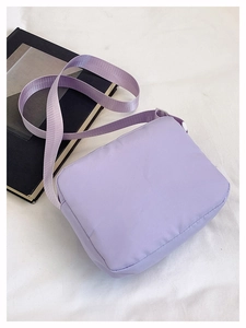 Detail shot of a minimalist light purple nylon crossbody bag on a textured white fabric background