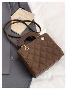 Detail of a brown quilted leather handbag with arched handles and gold hardware accents