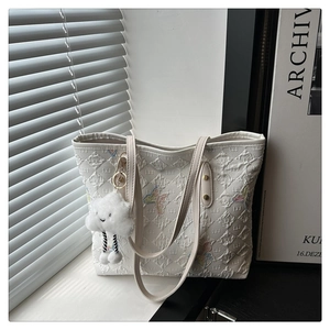 Detail of white quilted tote bag featuring colorful butterfly embroidery and cloud charm