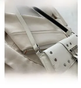 Detail of white patent leather shoulder bag featuring silver rivets and metallic buckle