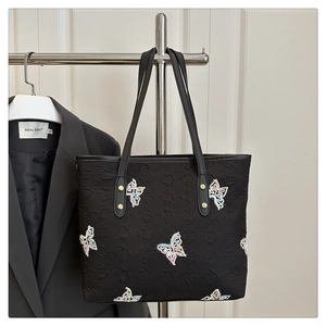 Detail of black tote bag featuring embroidered butterfly patterns and metal rivet accents