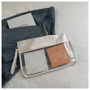 Flat lay of a transparent PVC makeup bag with white trim and gold zipper on denim fabric