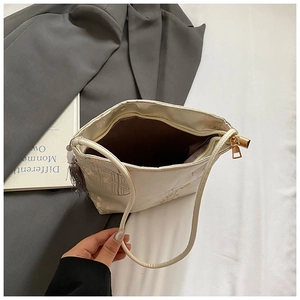 Detailed view of cream embroidered shoulder bag with tassel and dark brown lining
