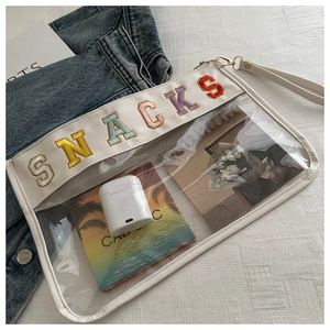 Detail of transparent PVC makeup bag with SNACKS embroidery and cream leather trim
