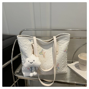 Detail of white quilted tote bag with colorful butterfly embroidery and cloud charm
