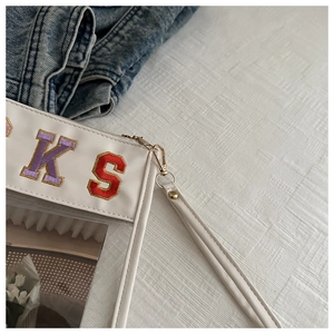 Detail of white leather makeup bag with colorful embroidered letters and clear window