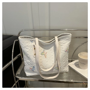 Detail of white tote bag featuring intricate butterfly embroidery and quilted texture