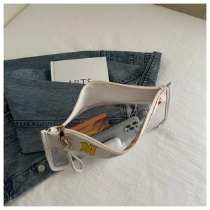 Detail of white semi-transparent PVC cosmetic bag with yellow N patch on denim background