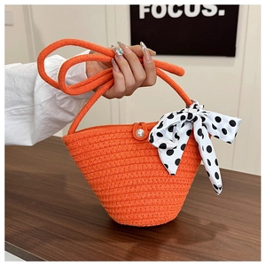 Detail of orange woven straw bucket bag featuring a pearl clasp and polka dot bow ribbon