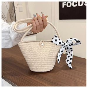 Detail of a beige straw crescent handbag featuring pearl button and polka dot silk scarf