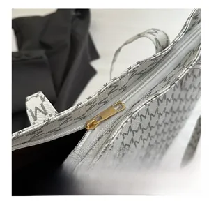 Close-up of golden metal zipper and monogram pattern on white large tote bag