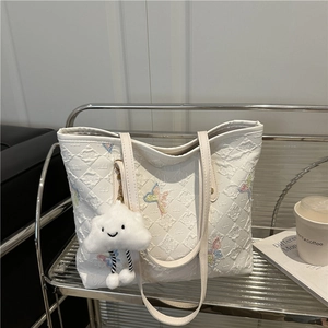 Quilted white tote bag with colorful butterfly embroidery and cloud charm on a shelf