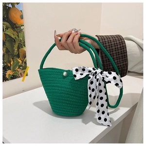 Detail of green woven bucket bag featuring a pearl clasp and black polka dot silk scarf