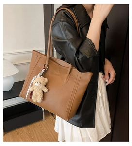 Brown lychee grain tote bag with plush bear charm worn on shoulder with a leather jacket