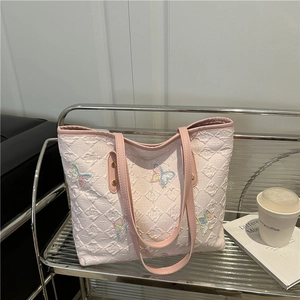 Pink tote bag with colorful butterfly embroidery and quilted texture on a metal stand