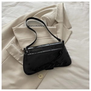 Detail of glossy black patent leather shoulder bag with adjustable strap on beige suit