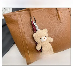 Detailed view of beige plush bear charm with red woven strap on a brown leather tote