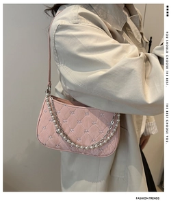 Détail d'un sac baguette matelassé rose avec chaîne en perles et broderie de nœuds