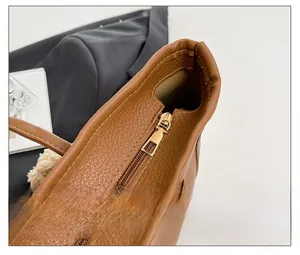 Detailed close-up of smooth gold metal zipper on brown leather tote bag with pebble grain