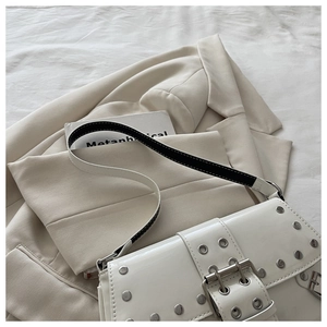 Detail of white patent leather shoulder bag with silver rivets on beige blazer