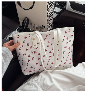 Detail of white tote bag featuring red cherry prints and faux leather texture in car setting