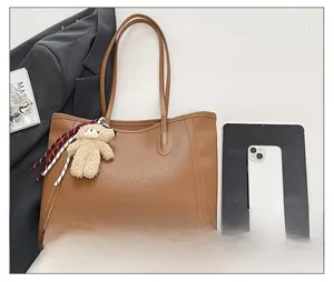 Flat lay detail of brown pebble leather tote bag featuring a cute plush bear pendant