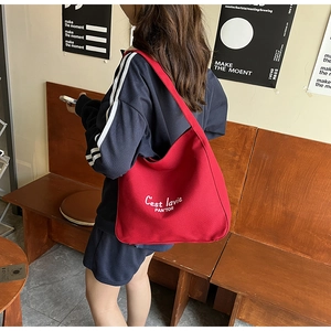 Detail shot of a red canvas tote bag with white embroidery worn by a model in a cafe