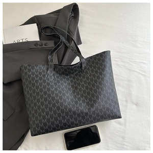 Detail of black tote bag featuring repetitive M letter print and durable shoulder straps