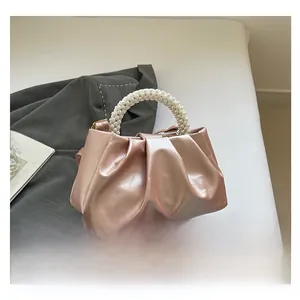 Close-up of pink satin cloud bag with elegant pearl handle on a blazer background