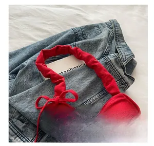Détail du sac à main en tissu rouge avec poignée plissée et nœud sur fond en denim