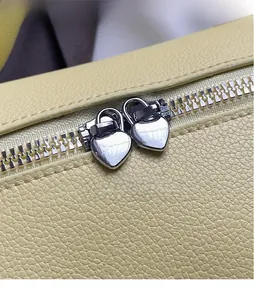 Close-up of litchi leather bag with silver heart-shaped zipper pulls and fine texture