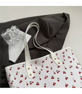 Detail of white cherry print tote bag featuring gold rivets and elegant leather texture