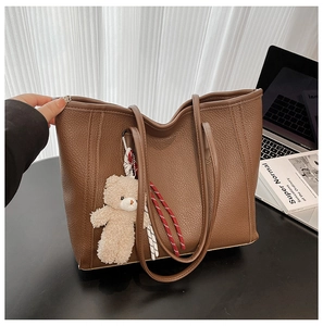 Detail of a brown lychee pattern leather tote bag with a plush bear charm and woven rope