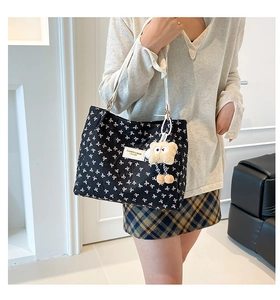 Détail d'un sac cabas noir à motifs de nœuds blancs avec un pendentif ours en peluche