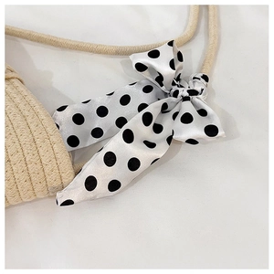 Close-up of woven straw handbag with a decorative polka dot silk scarf on the handle