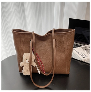 Close-up of deep brown pebbled leather tote bag with white plush bear and woven keychain