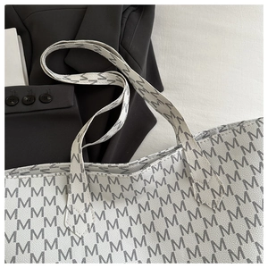 Close-up of minimalist white tote bag with grey M letter pattern and textured surface