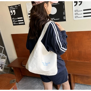 Close-up of white canvas tote bag featuring blue letter embroidery and sturdy handle