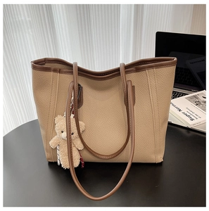 Close-up of beige lychee texture tote bag with brown straps and plush bear charm