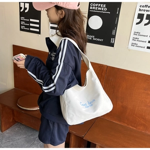 Close-up of white canvas tote bag with blue lettering on a wide shoulder strap