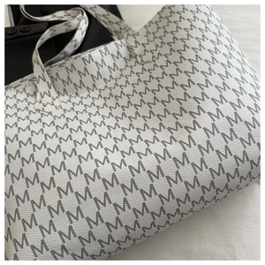 Close-up of white tote bag with black M letter print and textured faux leather detail