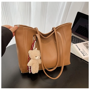 Detail of dark brown leather tote bag with lychee texture and plush bear pendant