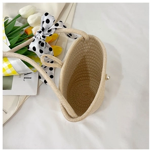 Detail view of woven straw beach bag with polka dot ribbon and pearl accent on white linen