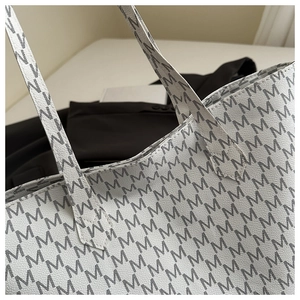 Detail of white tote bag with black letter M print and reinforced shoulder strap stitching