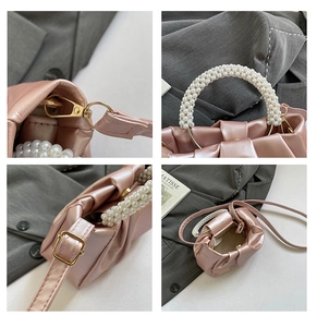 Detail view of pink pleated cloud bag featuring pearl handle and gold metal hardware