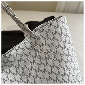 Close-up of letter M monogram pattern on white pebbled leather tote bag with V-stitching