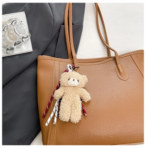 Gros plan d'un pendentif ours en peluche beige avec corde tressée sur un sac cabas